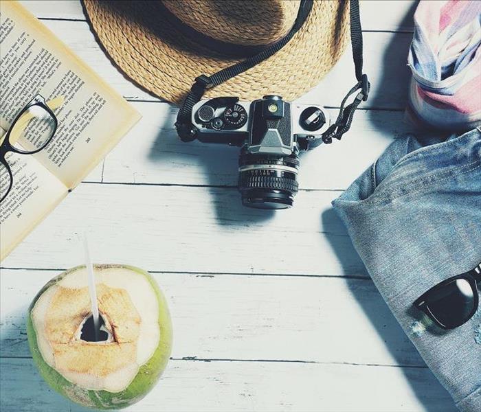 Wood flooring with books, glasses, hat, camera, clothes, and a vacation drink